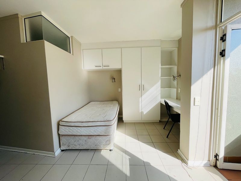 A functional bedroom featuring built-in cabinetry, a desk area, tiled flooring, and a transom window providing natural light.