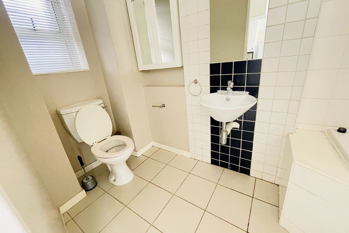 A functional bathroom featuring a wall-mounted basin, toilet, tiled flooring, and a tiled splashback with a built-in medicine cabinet.