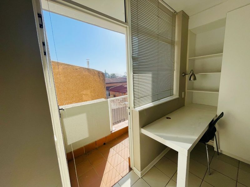 A functional home office space featuring a built-in desk, integrated shelving, and direct access to a private balcony.
