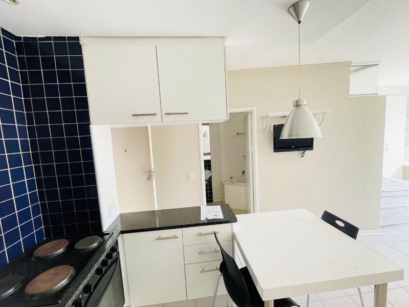 Compact kitchen featuring built-in cabinetry, granite countertops, and an electric stove, with a tiled backsplash and adjacent dining area.