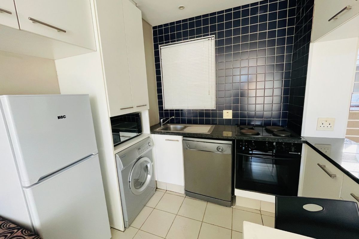 Compact kitchen featuring dark tiled backsplash, built-in oven and hob, stainless steel sink, and integrated cabinetry with space for laundry and dishwasher appliances.