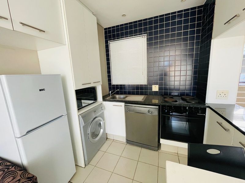 Compact kitchen featuring dark tiled backsplash, built-in oven and hob, stainless steel sink, and integrated cabinetry with space for laundry and dishwasher appliances.