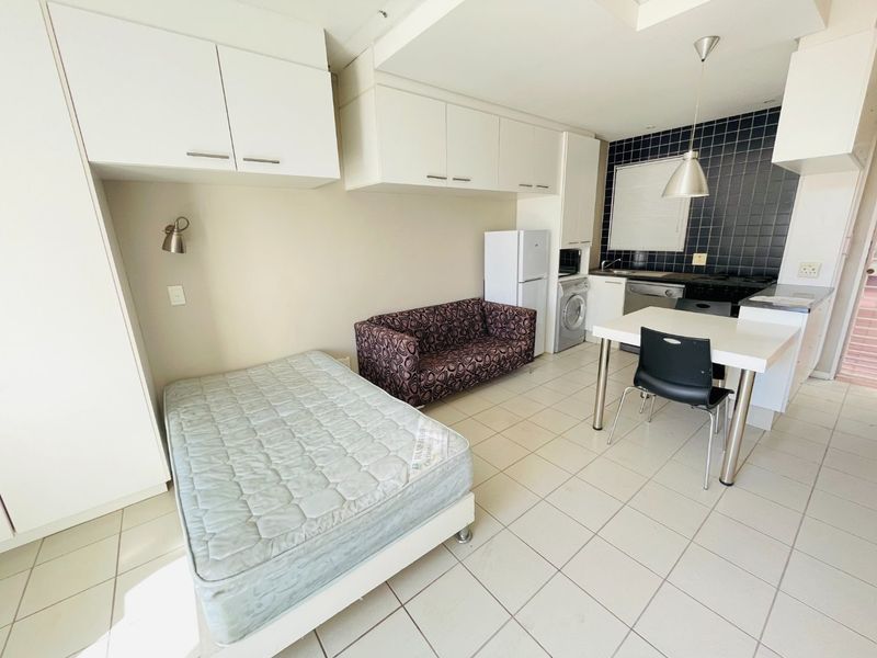 Open-plan studio apartment featuring a compact kitchen with tiled backsplash, built-in cabinetry, and tiled flooring throughout.