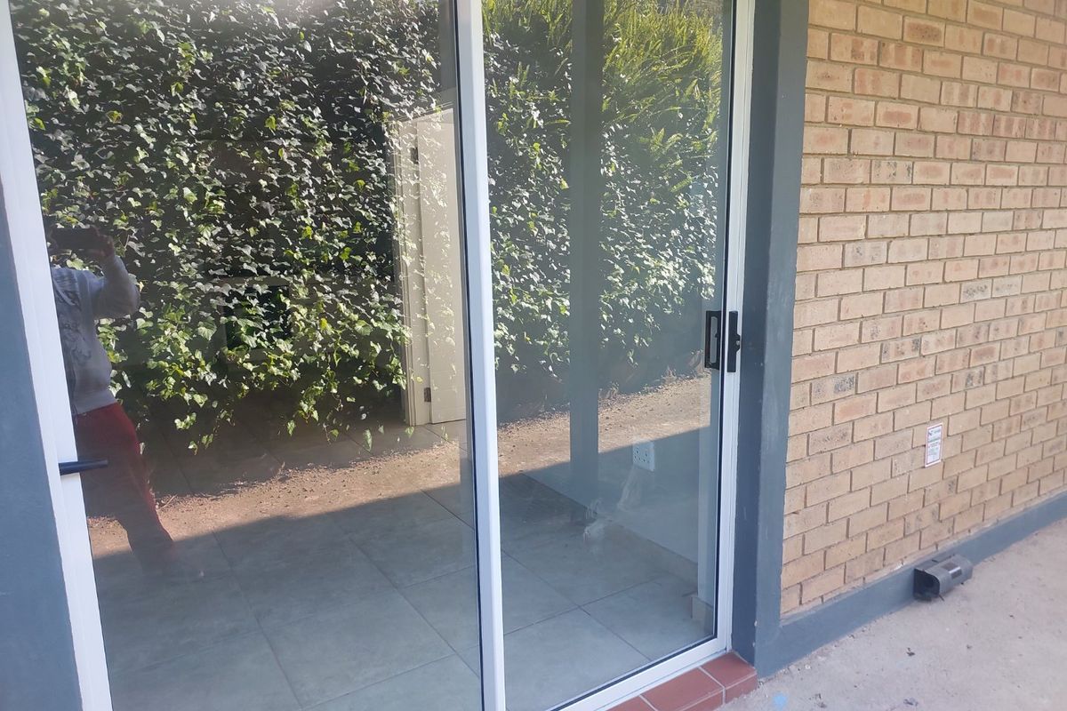 A view of a patio area featuring a sliding glass door, brick exterior wall, and tiled flooring.