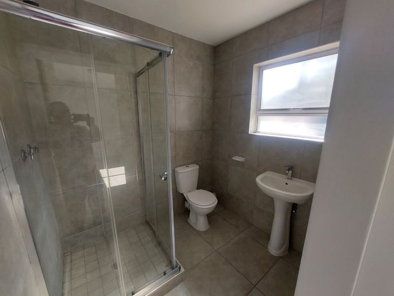 A clean, modern bathroom featuring a glass-enclosed shower, pedestal basin, and toilet with neutral floor-to-ceiling tiling.