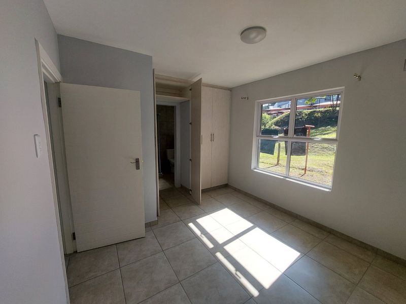 A bright, empty bedroom featuring tiled flooring, built-in cupboards, and an en-suite bathroom access point, offering a clean and neutral living space.