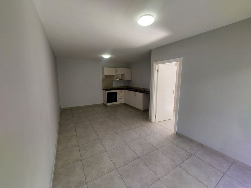 An open-plan living and kitchen area featuring neutral tiled flooring, built-in cabinetry with an integrated oven, and a clean, minimalist aesthetic.