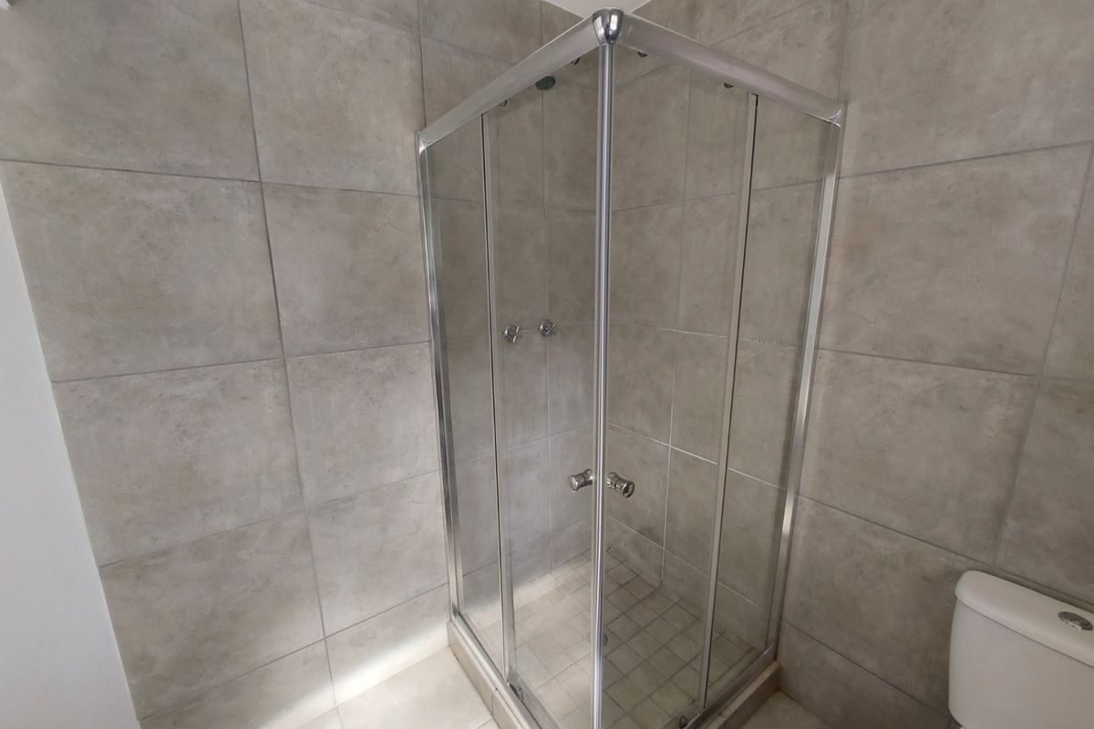 A clean, modern bathroom featuring a corner shower enclosure with glass doors and neutral ceramic wall and floor tiling.