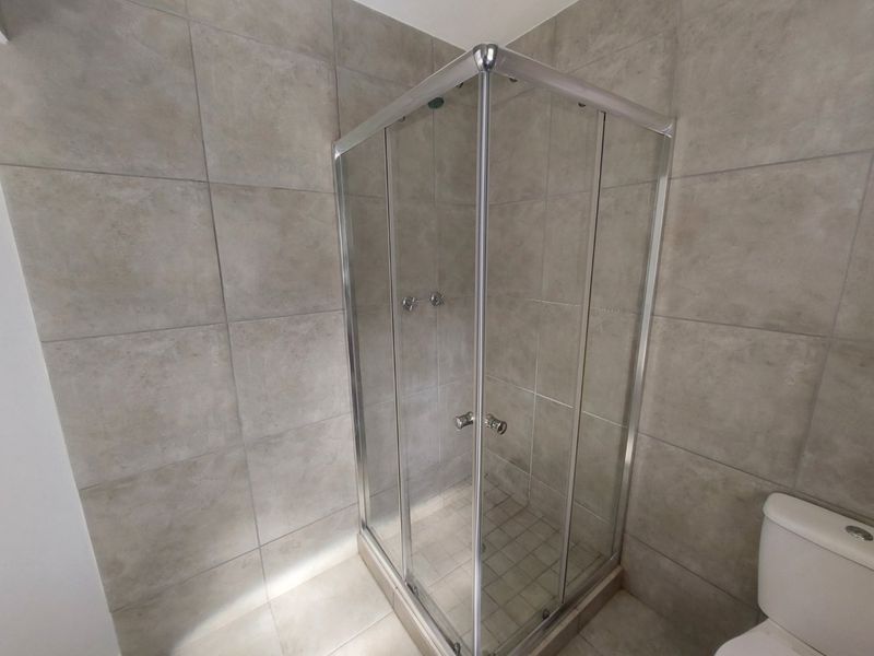 A clean, modern bathroom featuring a corner shower enclosure with glass doors and neutral ceramic wall and floor tiling.