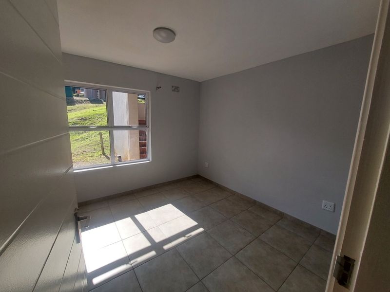 A clean, empty bedroom featuring neutral wall paint, tiled flooring, and a large window providing natural light.
