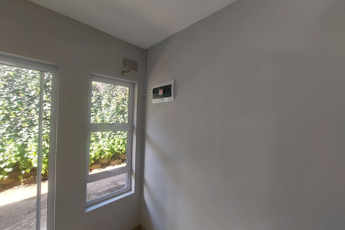 An empty, neutral-toned room featuring an aluminium sliding door, a window, and a wall-mounted electrical distribution board.