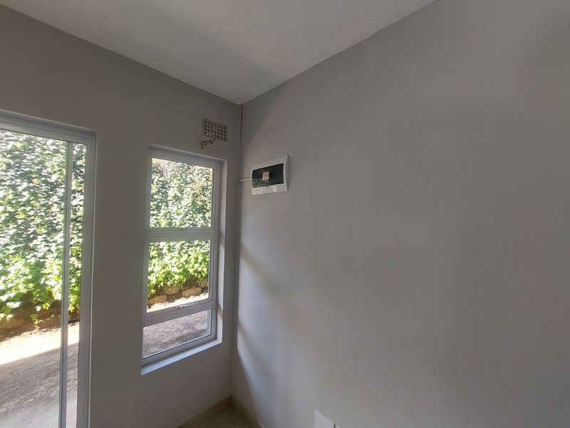 An empty, neutral-toned room featuring an aluminium sliding door, a window, and a wall-mounted electrical distribution board.