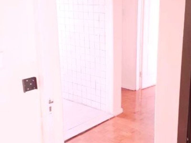 A bright hallway featuring classic parquet flooring and an arched entryway leading into a tiled space.