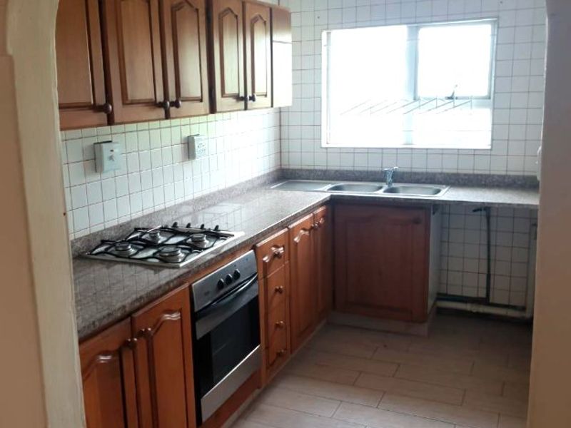 A functional kitchen featuring wooden cabinetry, granite countertops, a gas hob, built-in oven, and a double sink with tiled backsplash and flooring.