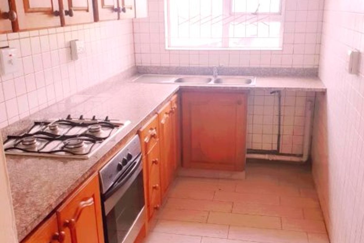 A functional kitchen featuring wooden cabinetry, granite countertops, a gas hob, built-in oven, and a double stainless steel sink with tiled splashbacks.