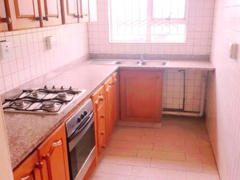 A functional kitchen featuring wooden cabinetry, granite countertops, a gas hob, built-in oven, and a double stainless steel sink with tiled splashbacks.