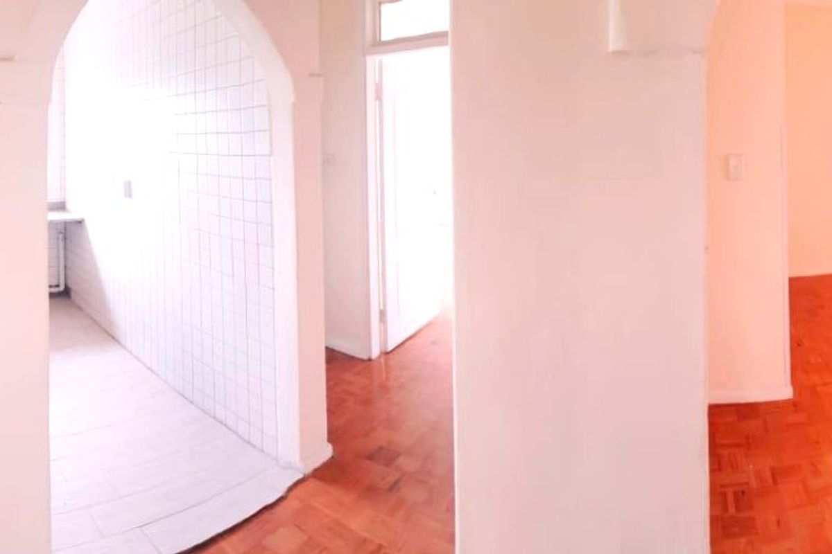 A bright, empty hallway featuring classic parquet flooring and a distinctive arched entryway leading to a tiled utility or kitchen space.