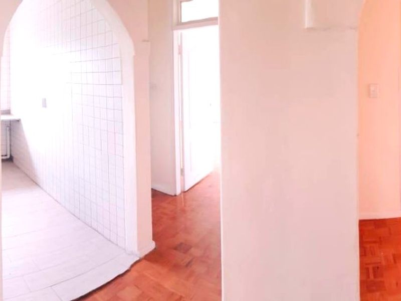 A bright, empty hallway featuring classic parquet flooring and a distinctive arched entryway leading to a tiled utility or kitchen space.