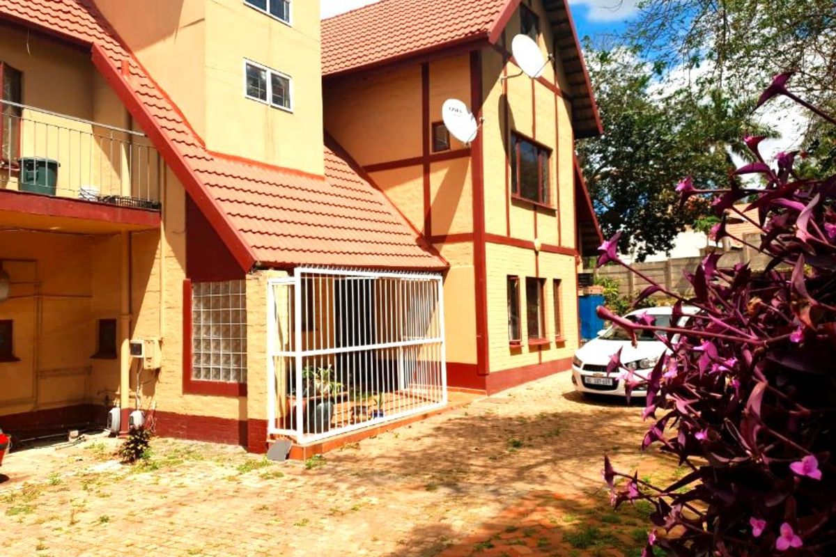 Rear view of a multi-story apartment building featuring a tiled roof, security gate, and paved driveway area.