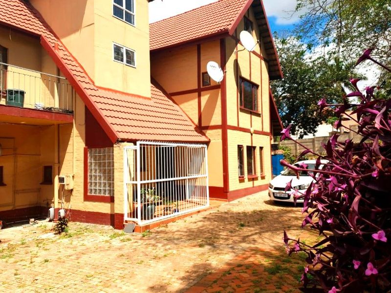 Rear view of a multi-story apartment building featuring a tiled roof, security gate, and paved driveway area.