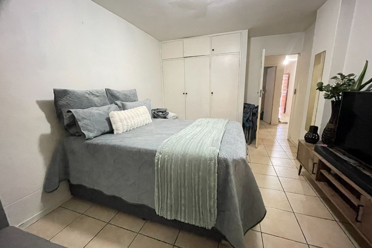 A functional bedroom featuring built-in cupboards and tiled flooring, offering a practical layout with direct access to the hallway.