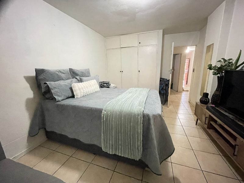A functional bedroom featuring built-in cupboards and tiled flooring, offering a practical layout with direct access to the hallway.