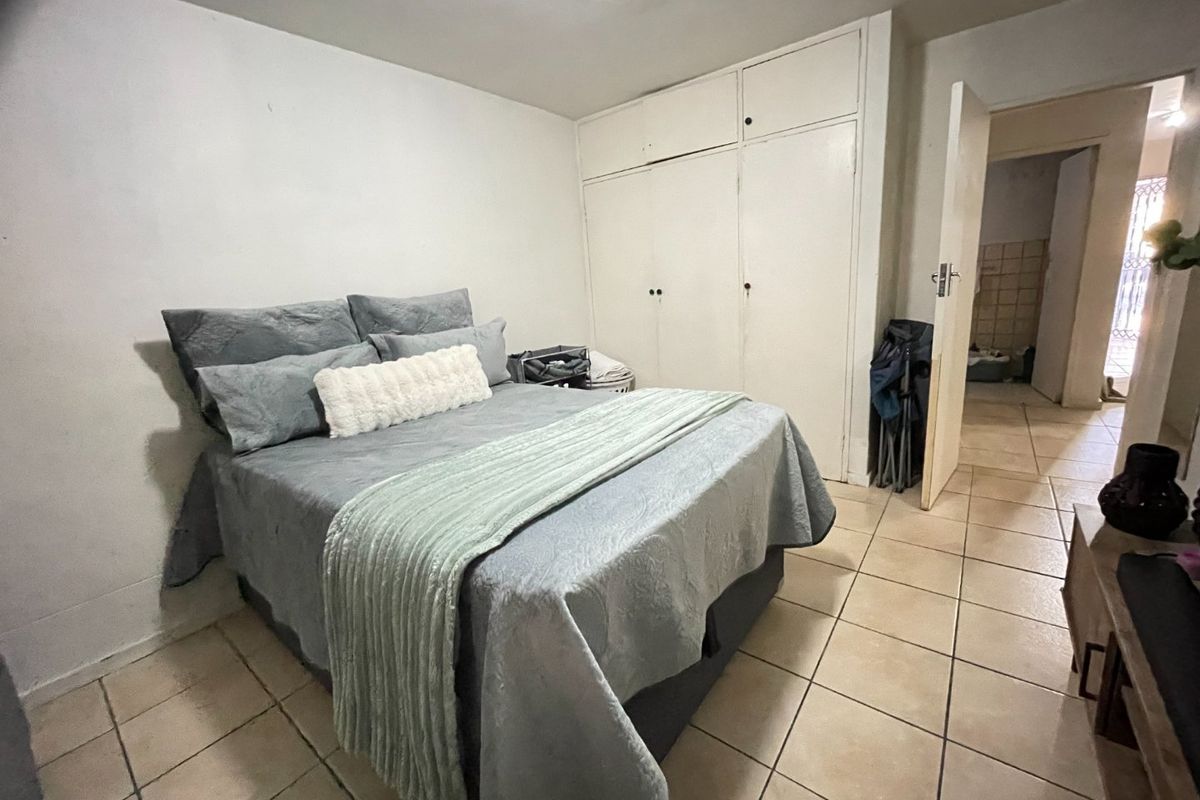 A bedroom featuring tiled flooring and built-in cupboards, offering a functional space with potential for cosmetic updates to enhance its overall appeal.