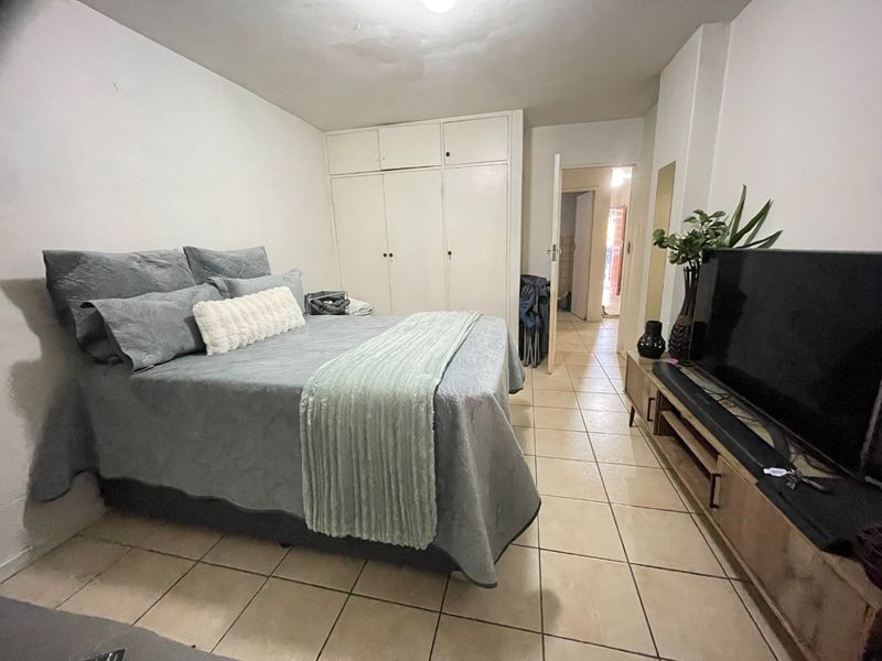 A bedroom featuring built-in cupboards and tiled flooring, providing a functional space with direct access to the hallway.