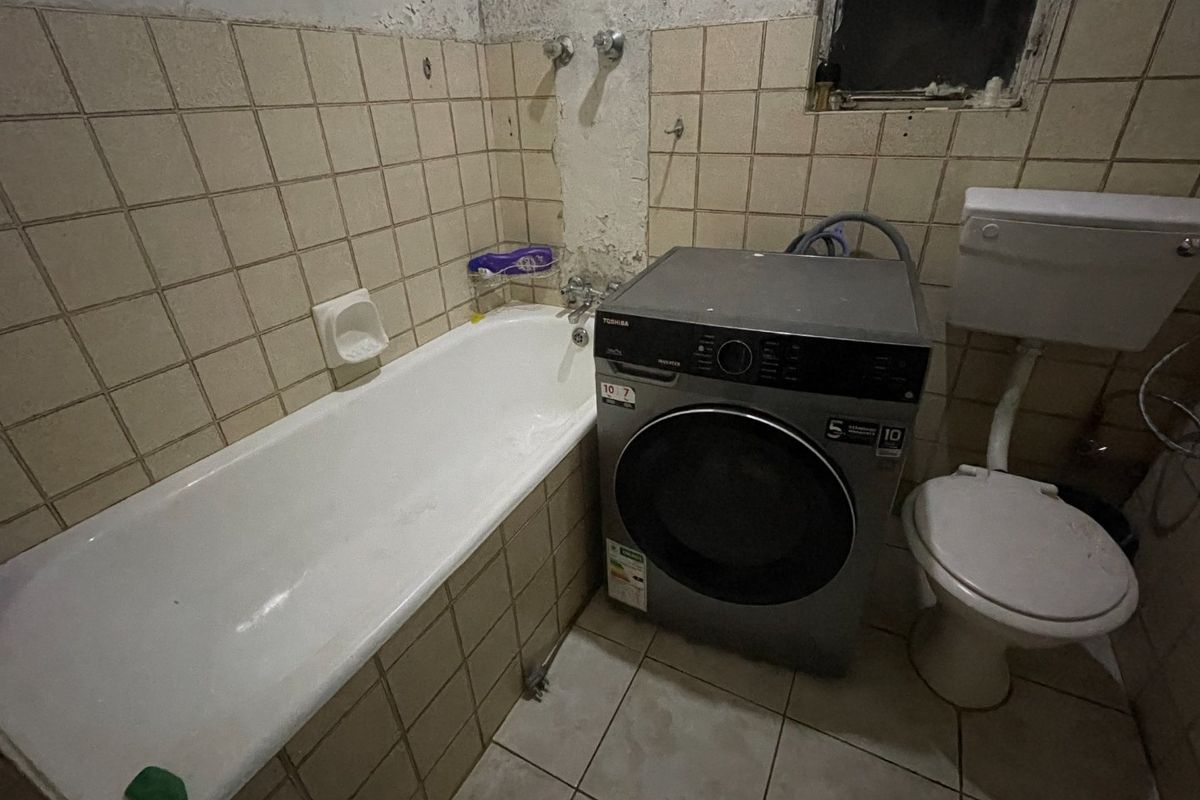 A dated bathroom featuring a bathtub, toilet, and tiled surfaces, currently showing significant wear and requiring renovation to improve the overall condition.