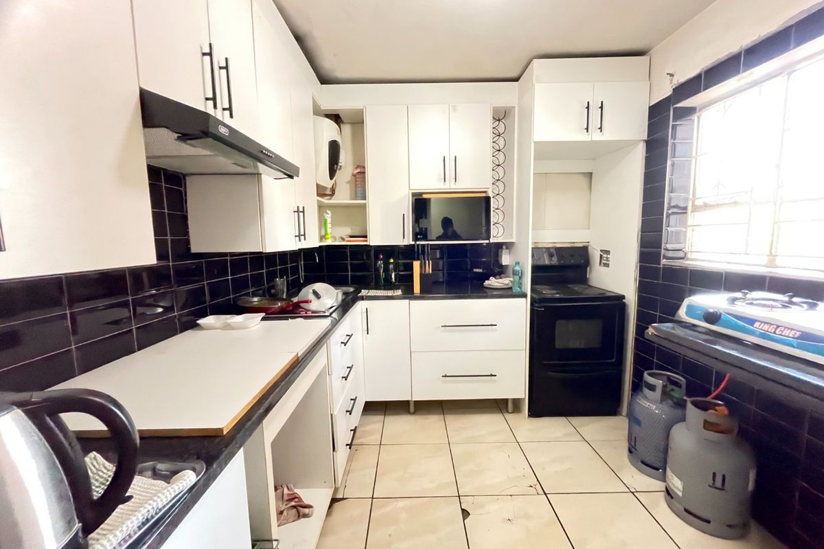 A functional kitchen featuring white cabinetry, black tiled backsplash, tiled flooring, and built-in oven with extractor fan.