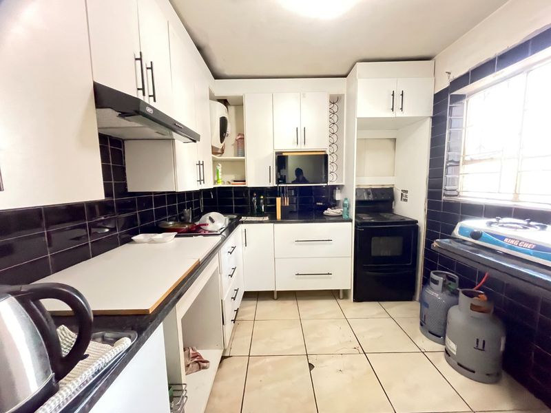 A functional kitchen featuring white cabinetry, black tiled backsplash, tiled flooring, and built-in oven with extractor fan.