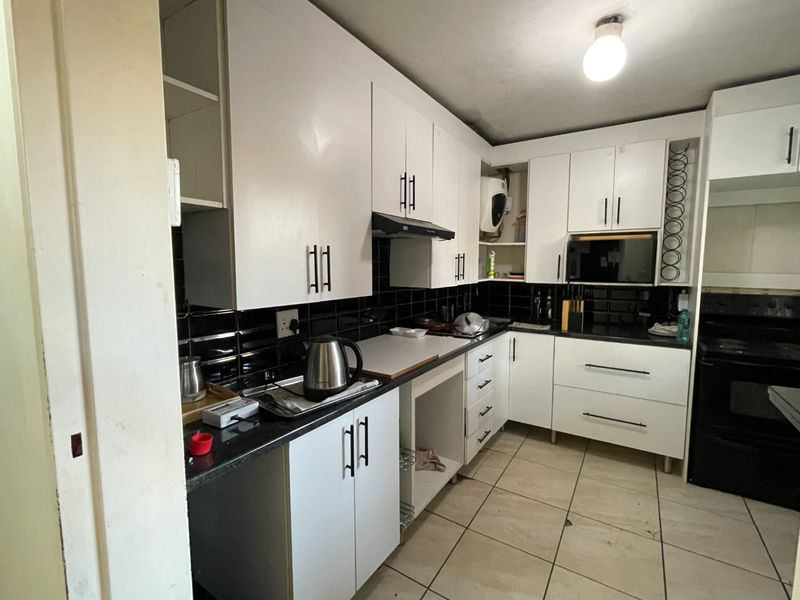 A functional kitchen featuring white cabinetry, black tiled backsplash, dark countertops, and tiled flooring, providing a practical workspace with integrated appliances.