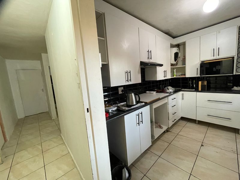 A functional kitchen featuring white built-in cabinetry, black tiled backsplash, and tiled flooring, adjacent to a hallway entrance.