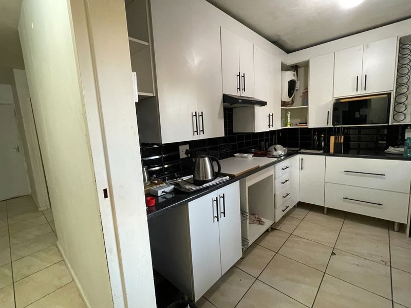 A functional kitchen featuring white cabinetry, black subway tile backsplash, dark countertops, and tiled flooring, offering a clean and practical workspace.
