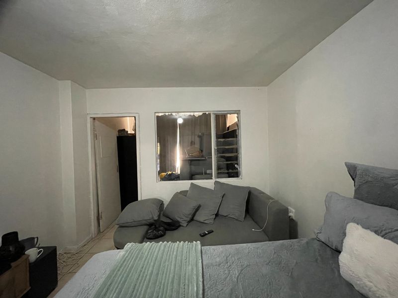 A bedroom featuring tiled flooring and an internal window looking into an adjacent space, requiring cosmetic updates to wall and ceiling finishes.
