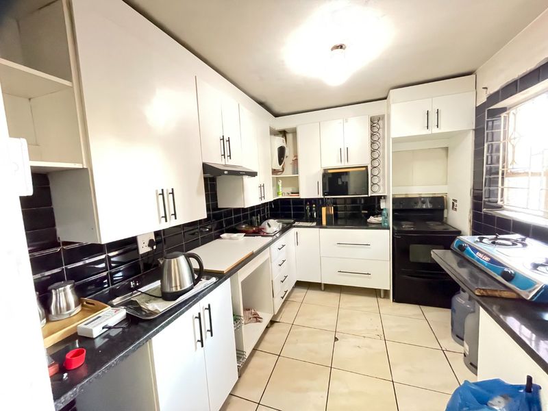 A functional kitchen featuring white cabinetry, black subway tile backsplash, dark granite countertops, and ceramic floor tiles.