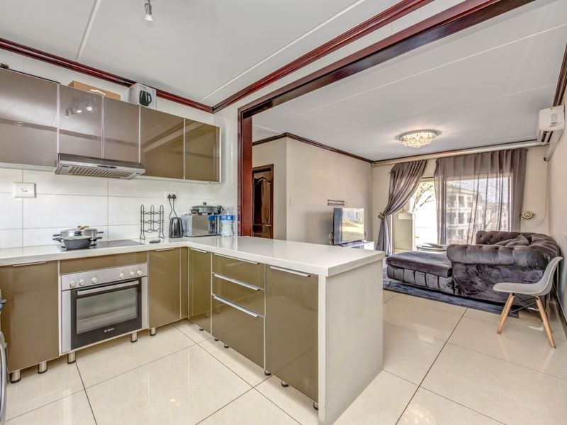 Open-plan kitchen and living area featuring modern cabinetry, stone countertops, integrated appliances, and tiled flooring throughout.