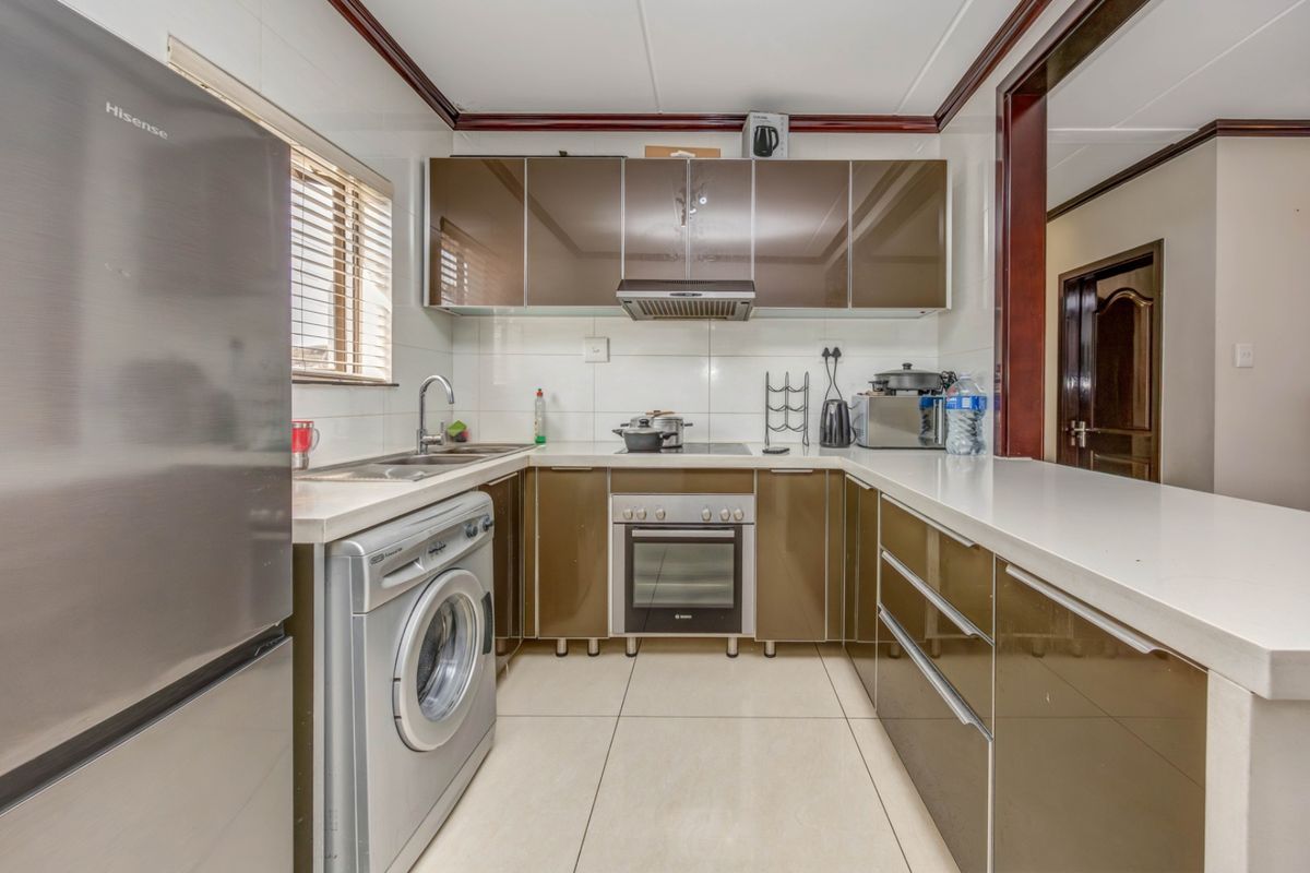 A functional kitchen featuring modern brown cabinetry, stone countertops, integrated oven, cooktop, extractor fan, and tiled finishes.