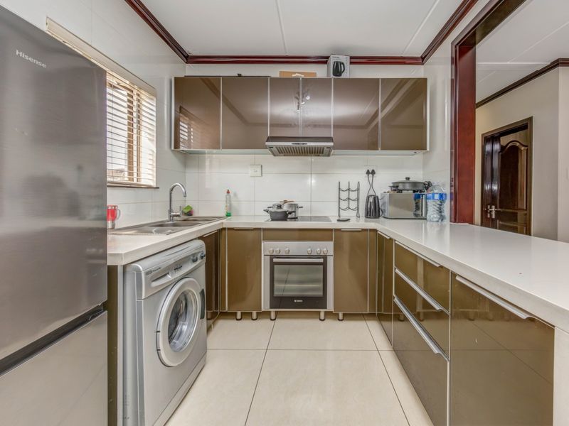 A functional kitchen featuring modern brown cabinetry, stone countertops, integrated oven, cooktop, extractor fan, and tiled finishes.