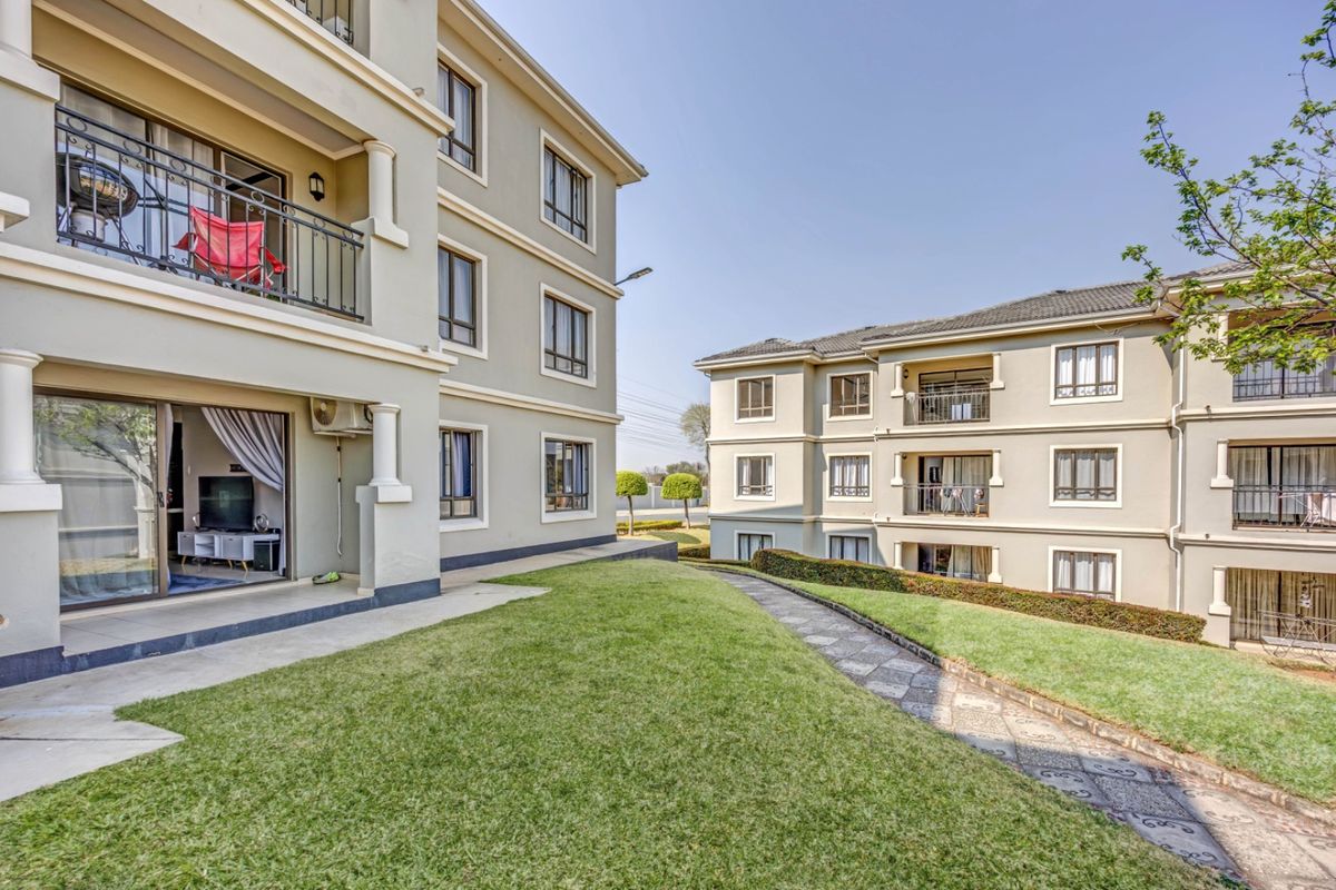 Exterior view of apartment complex buildings featuring balconies, sliding glass doors, and well-maintained communal lawn areas with stone pathways.