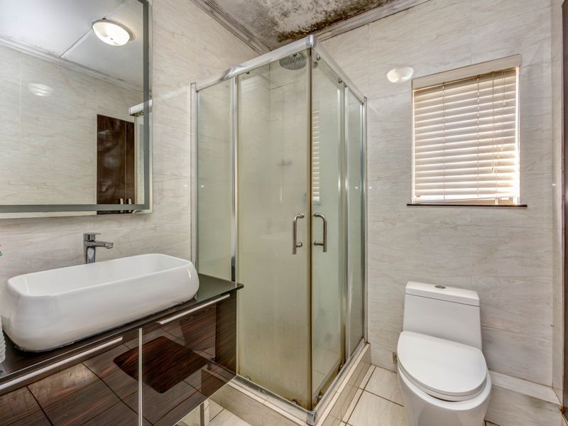 A compact bathroom featuring a vessel sink vanity, glass shower enclosure, and toilet, currently showing signs of ceiling water damage requiring repair.