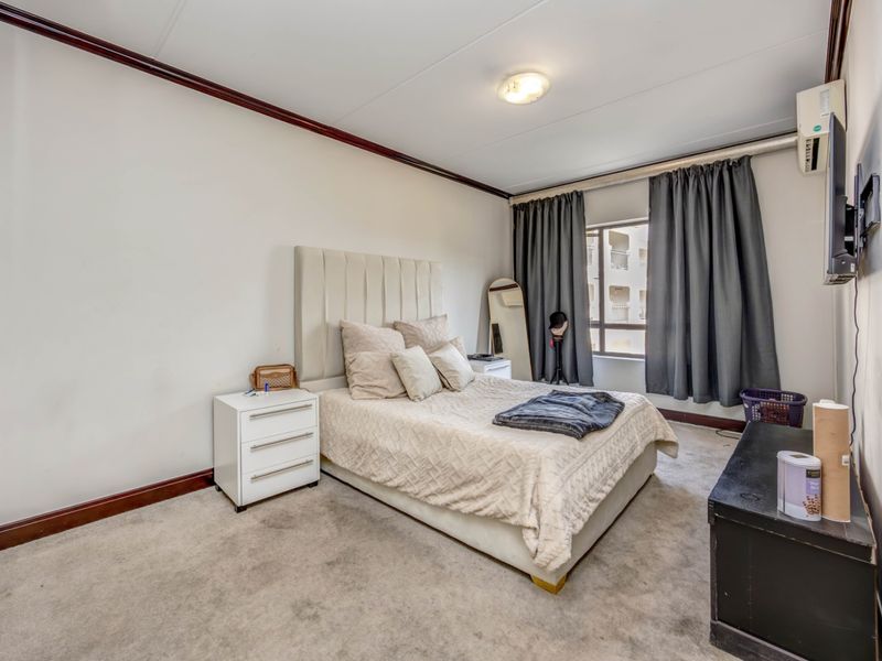 A well-proportioned bedroom featuring carpeted flooring, coving, and a wall-mounted air conditioning unit.