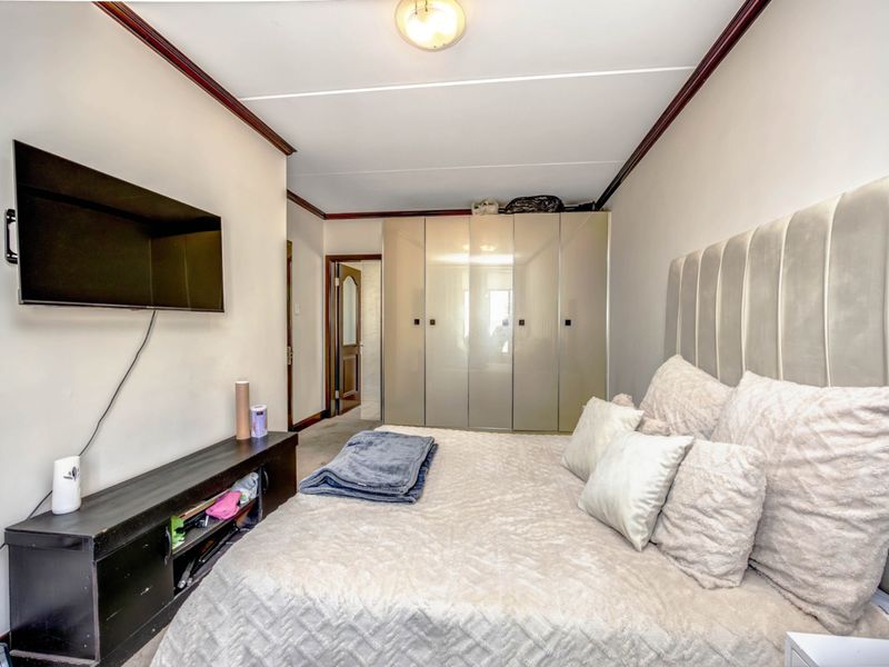 A bedroom featuring a built-in wardrobe with reflective doors, crown molding, and a neutral color palette.