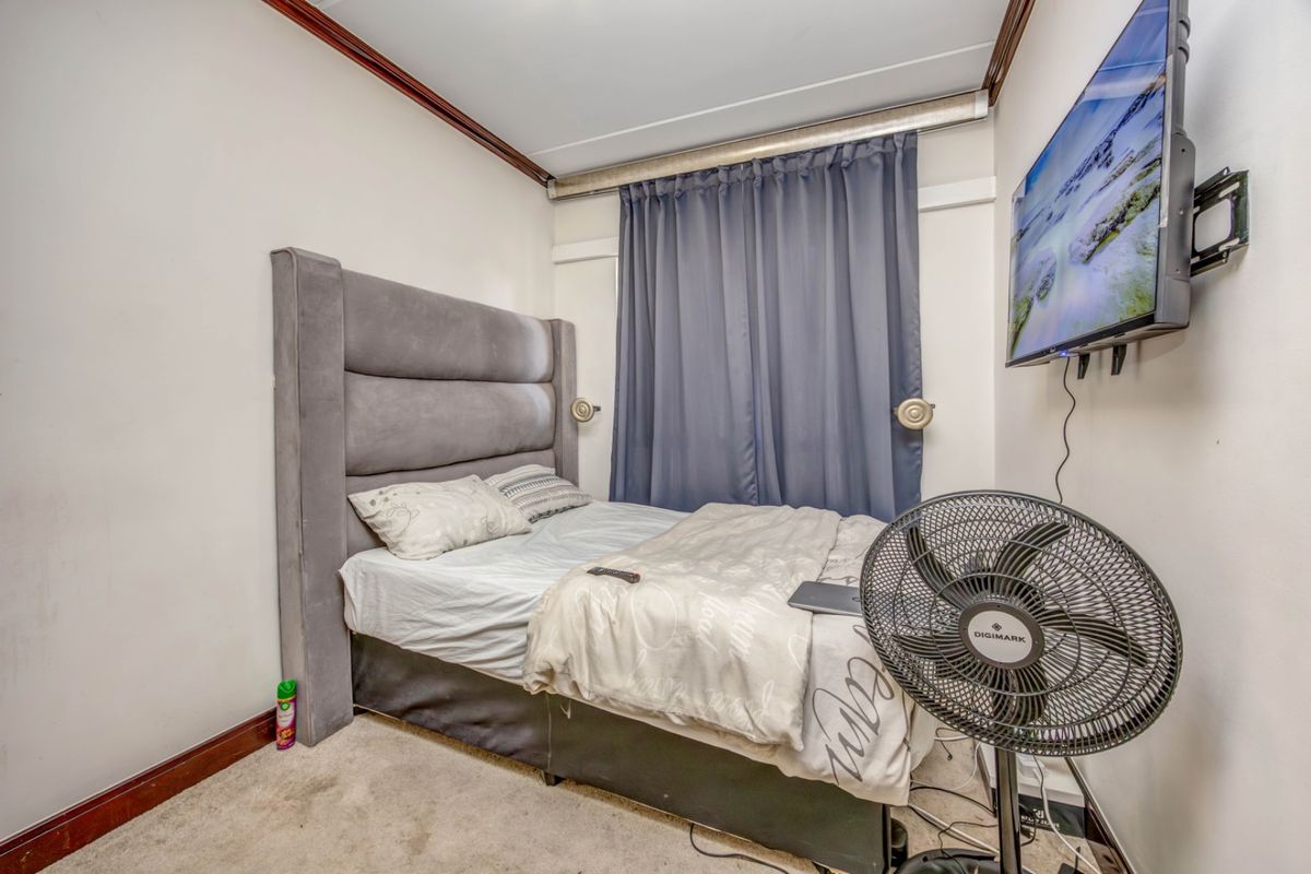A compact bedroom featuring carpeted flooring, crown molding, and a wall-mounted television bracket.