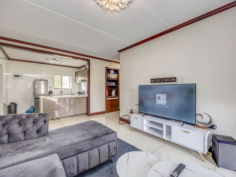 Open-plan living area featuring tiled flooring, a modern kitchen with island, and built-in shelving, creating a functional and connected living space.
