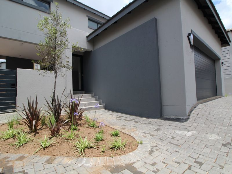 Modern front facade featuring a paved driveway, sectional garage door, and a landscaped garden bed leading to the main entrance.