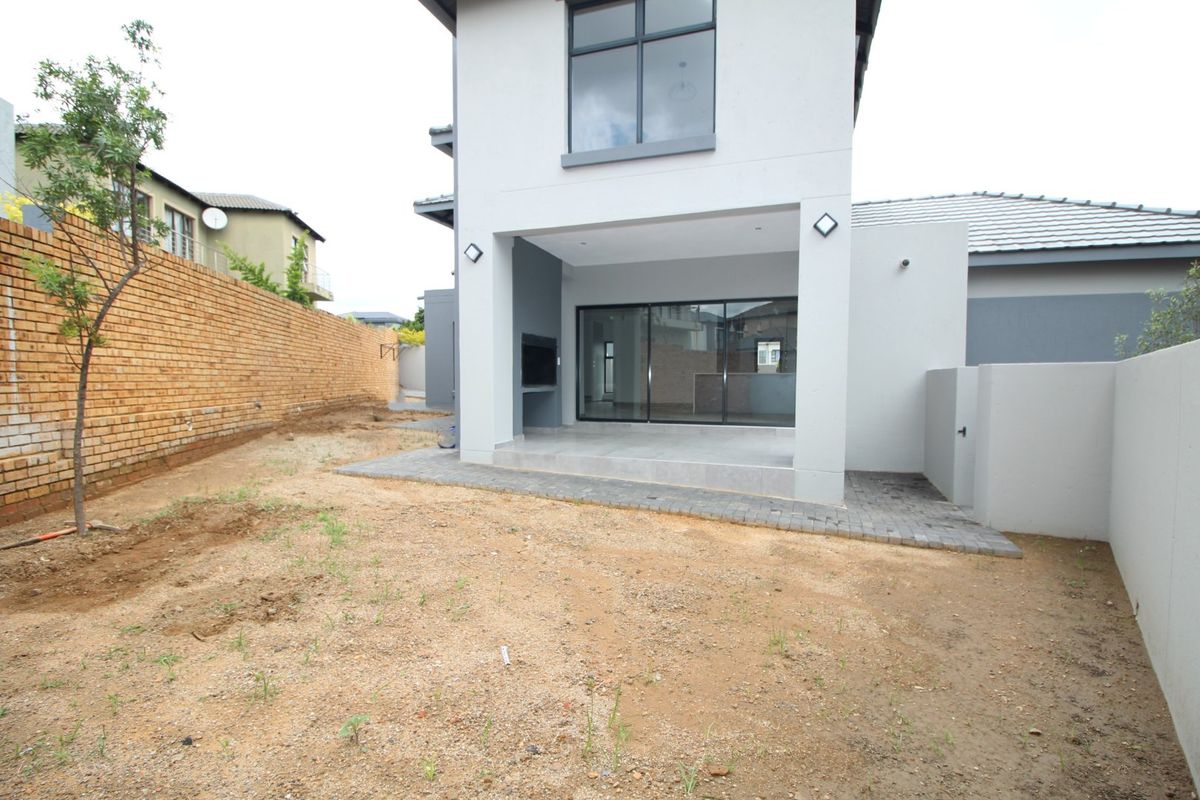 Rear view of the property featuring a covered patio with a built-in braai, sliding glass doors, and an expansive, unlandscaped garden area.