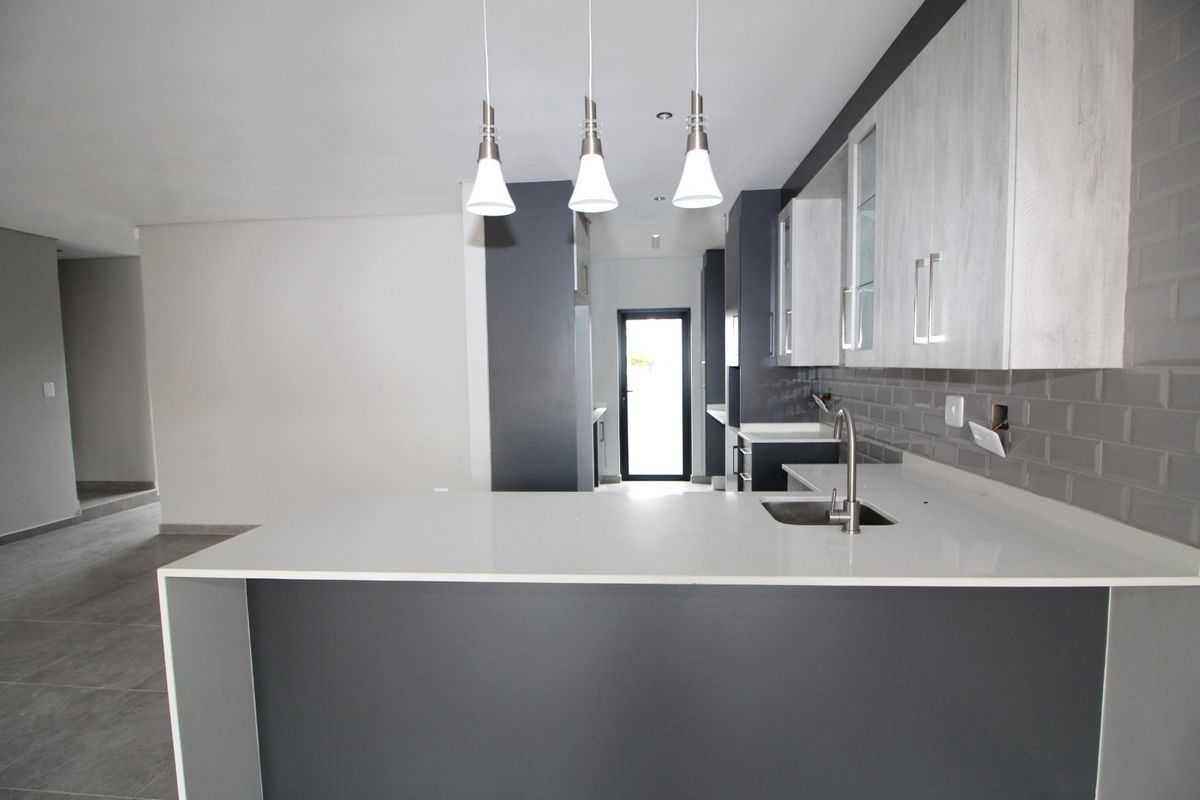 Modern kitchen featuring quartz countertops, subway tile backsplash, and sleek two-tone cabinetry with pendant lighting in an open-plan layout.