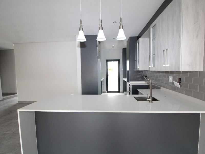 Modern kitchen featuring quartz countertops, subway tile backsplash, and sleek two-tone cabinetry with pendant lighting in an open-plan layout.