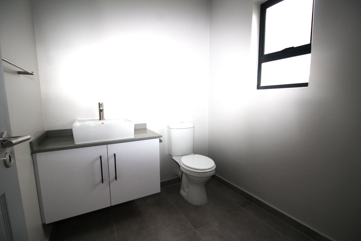 A clean, modern bathroom featuring a vanity with a vessel sink, a toilet, and neutral floor tiling.